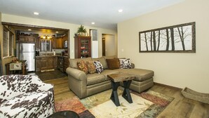 A living room with a sofa, a coffee table, and a rug. There is a kitchen visible in the background. - Gorgeous Lakeside hideout with views of the lake and mountains (Big Bear Lake)