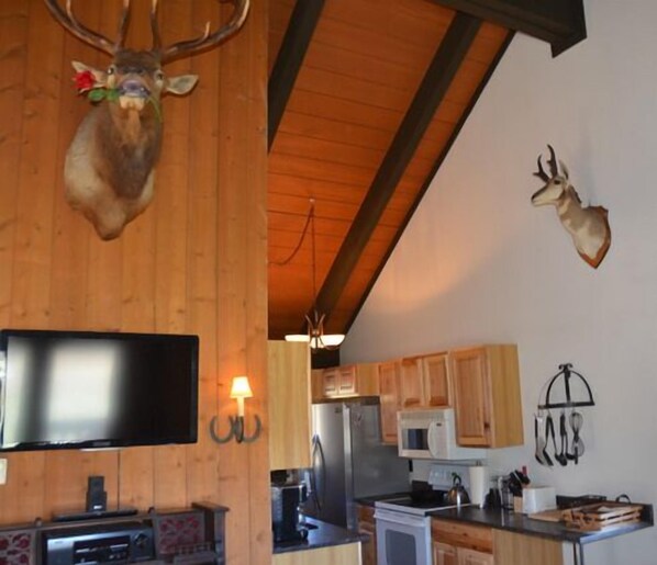 Una cocina con armarios de madera, microondas, refrigerador y televisor de pantalla plana montado en la pared.