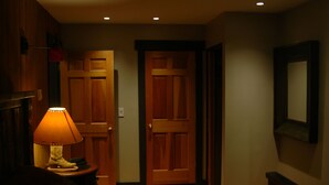 Une chambre d’hôtel avec une porte en bois, une lampe sur une table de chevet et un tableau encadré au mur.
