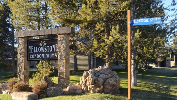 Une plaque en pierre indiquant « Yellowstone Condominiums » et un panneau de rue indiquant « Yellowstone Spur Rd. ».