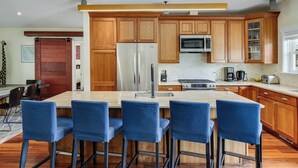 A modern kitchen with wooden cabinets, a stainless steel refrigerator, a microwave, and a large island with bar stools.