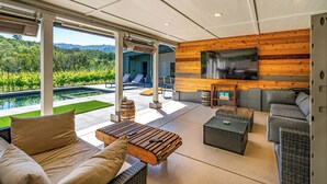 A modern outdoor living area with a pool, comfortable seating, and a large TV screen.