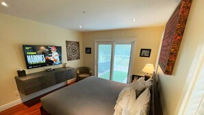 A bedroom with a bed, a TV on a dresser, a chair, and a balcony view.