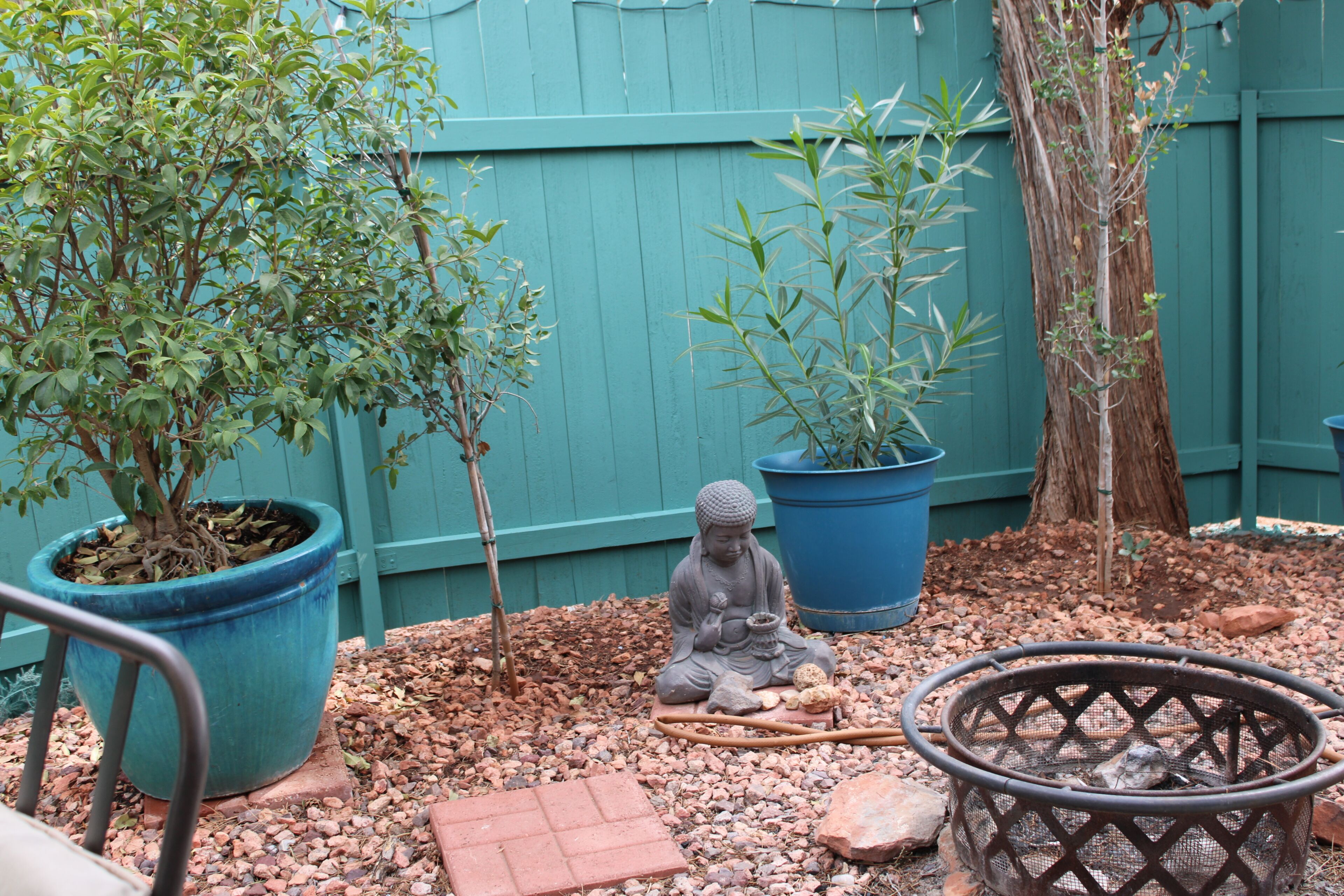 Un jardín con plantas en macetas, una estatua de Buda y una chimenea.