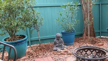 Un jardín con plantas en macetas, una estatua de Buda y una chimenea.