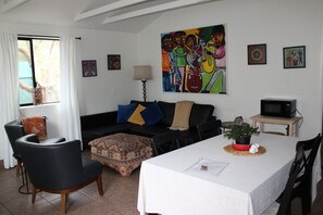 A living room with a sofa, a dining table, a TV, and a painting on the wall. - Red Rock Retreat: Hot tub, walk to creek for swimming,. (Sedona)
