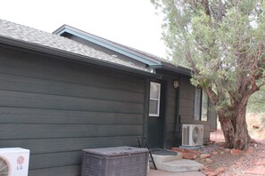 A house with a dark wooden exterior, a visible air conditioning unit, and a tree in the background. - Red Rock Retreat: Hot tub, walk to creek for swimming,. (Sedona)