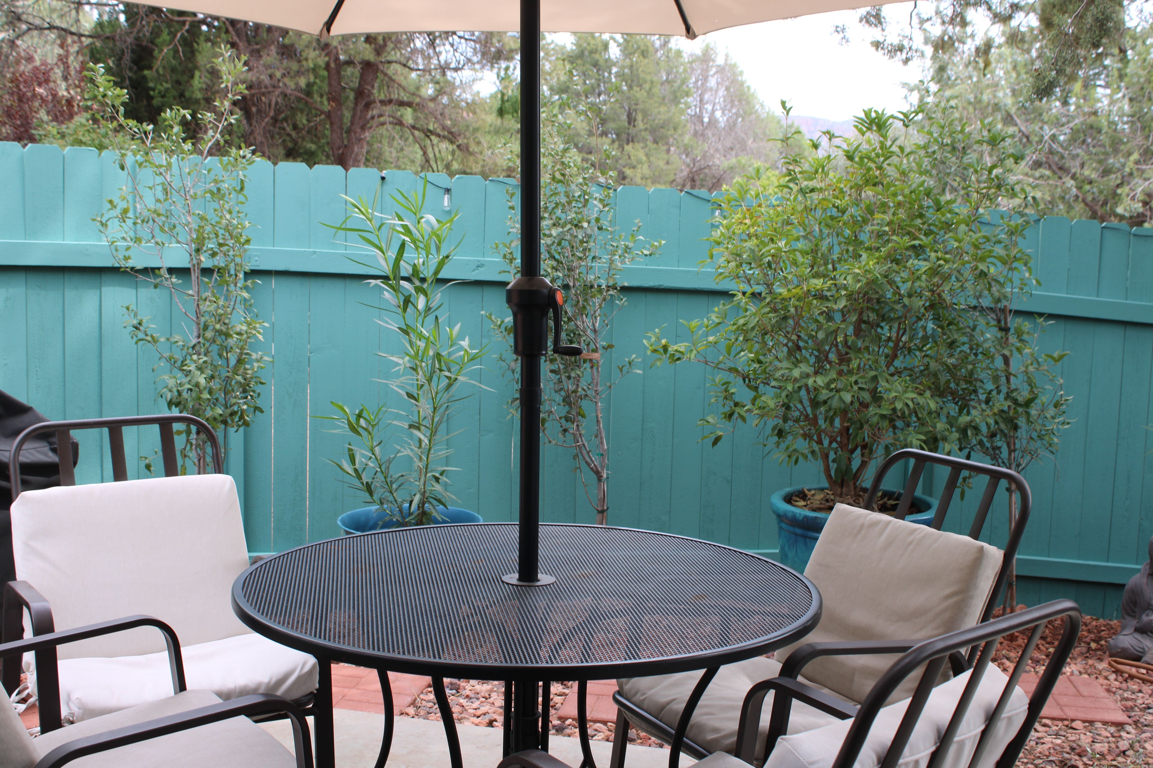 A round metal table with four chairs, a blue fence, and potted plants in a backyard setting.