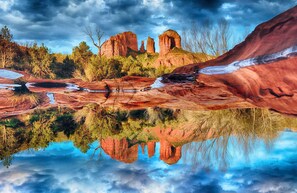Un paysage naturel où l’on peut admirer un reflet limpide dans une étendue d’eau, le tout étant bordé d’arbres et de formations rocheuses.