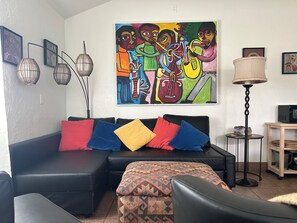A living room with a black sofa, colorful cushions, a patterned ottoman, a painting on the wall, a floor lamp, and a small side table with a lamp. - Red Rock Retreat: Hot tub, walk to creek for swimming,. (Sedona)