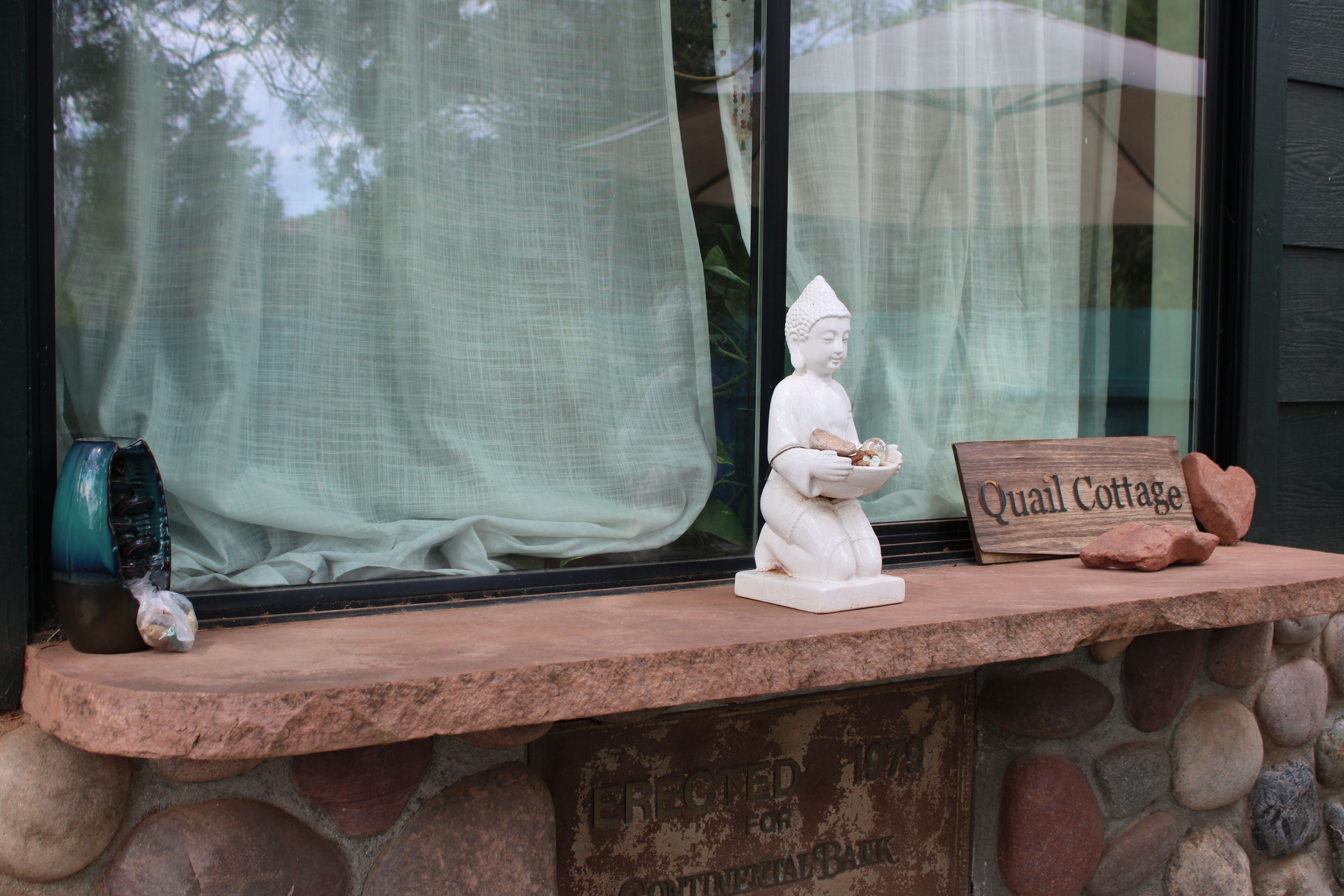 Eine Steinstufe mit einer Statue, einem Keramiktopf und einem Schild mit der Aufschrift 'Quail Cottage'.