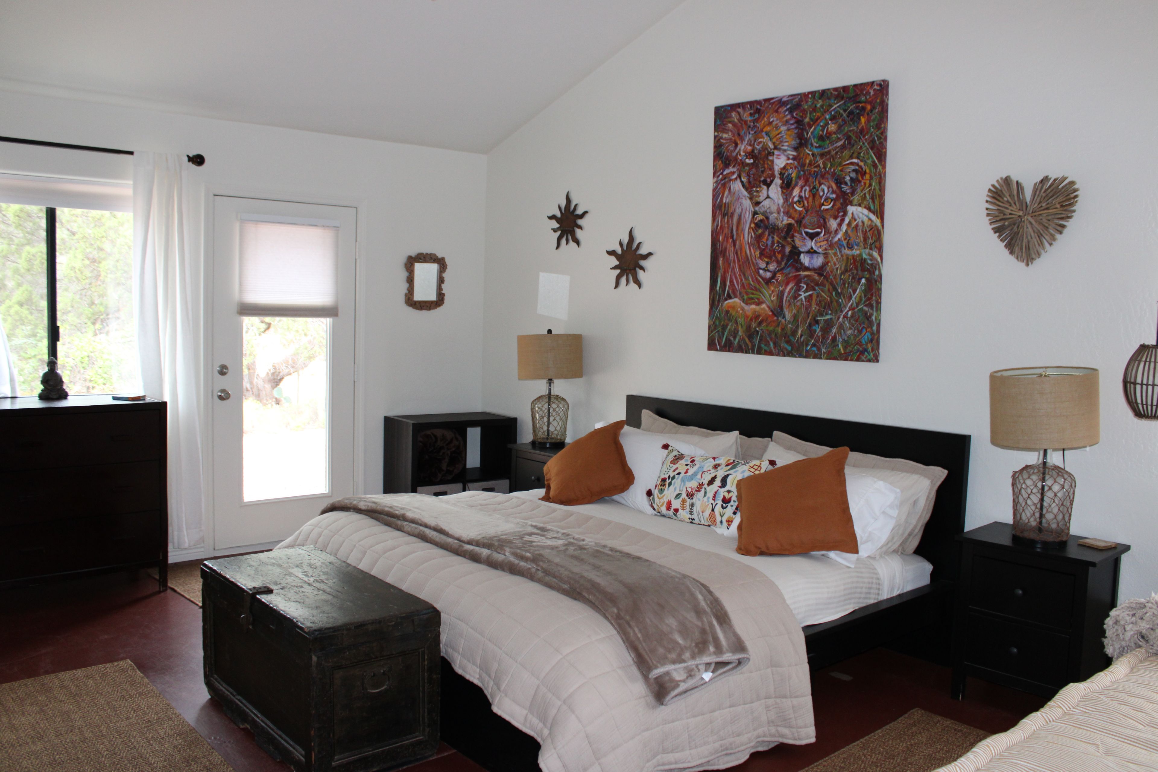 Een slaapkamer met een bed, nachtkastjes, een dressoir, een raam en een schilderij aan de muur.