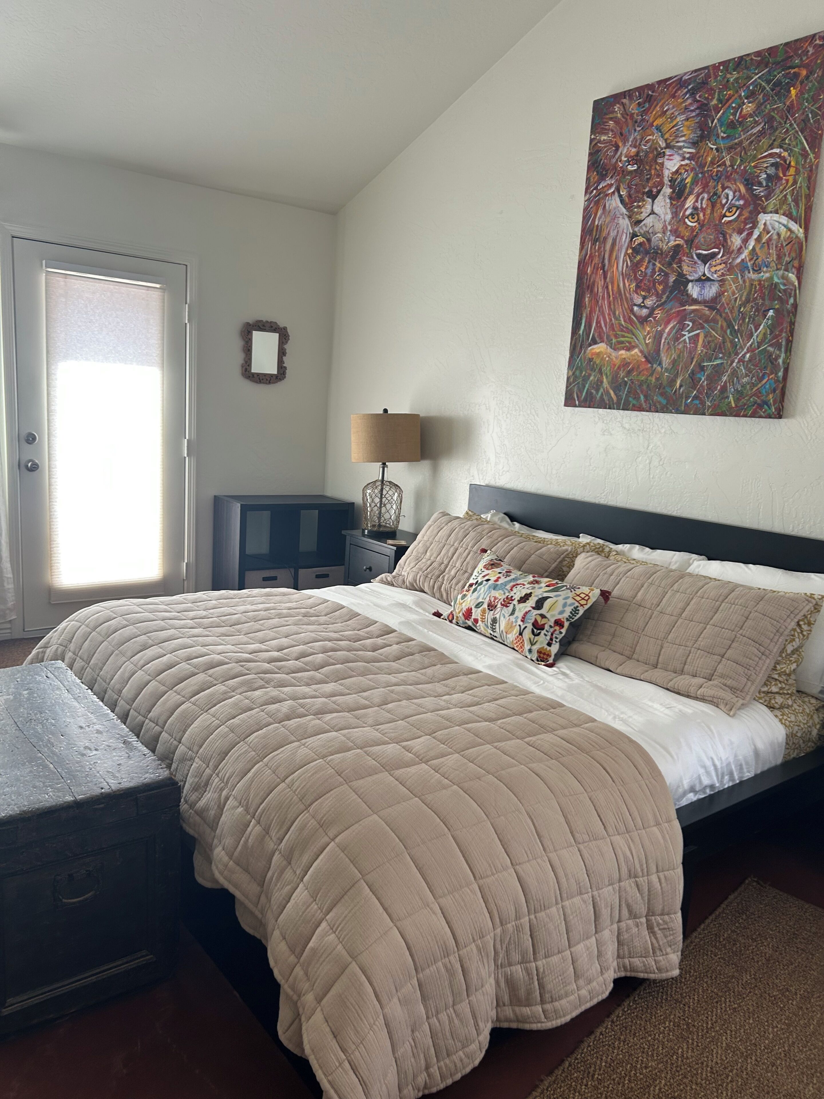 A bedroom with a bed, a nightstand, a lamp, a painting, and a door.
