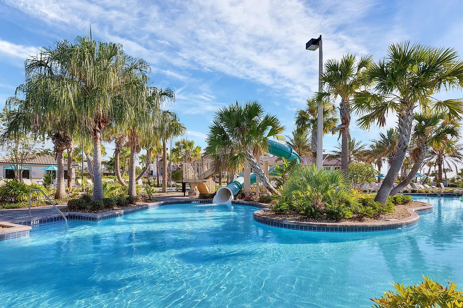 A swimming pool with a water slide, surrounded by palm trees and a clear sky.