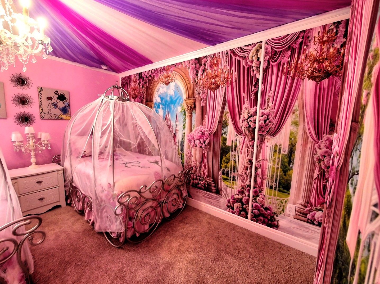 Ein zart rosa gestaltetes Schlafzimmer mit einem Himmelbett, einem Schminktisch und einer Wandmalerei eines Schlosses.