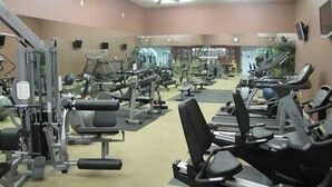 A gym with various exercise machines, mirrors, and ceiling fans.