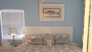 A bedroom with a bed, a nightstand, a lamp, a ceiling fan, and a framed picture on the wall.