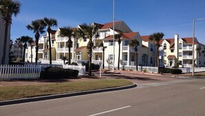 A row of coastal residential buildings with a white picket fence, palm trees, and a clear blue sky.