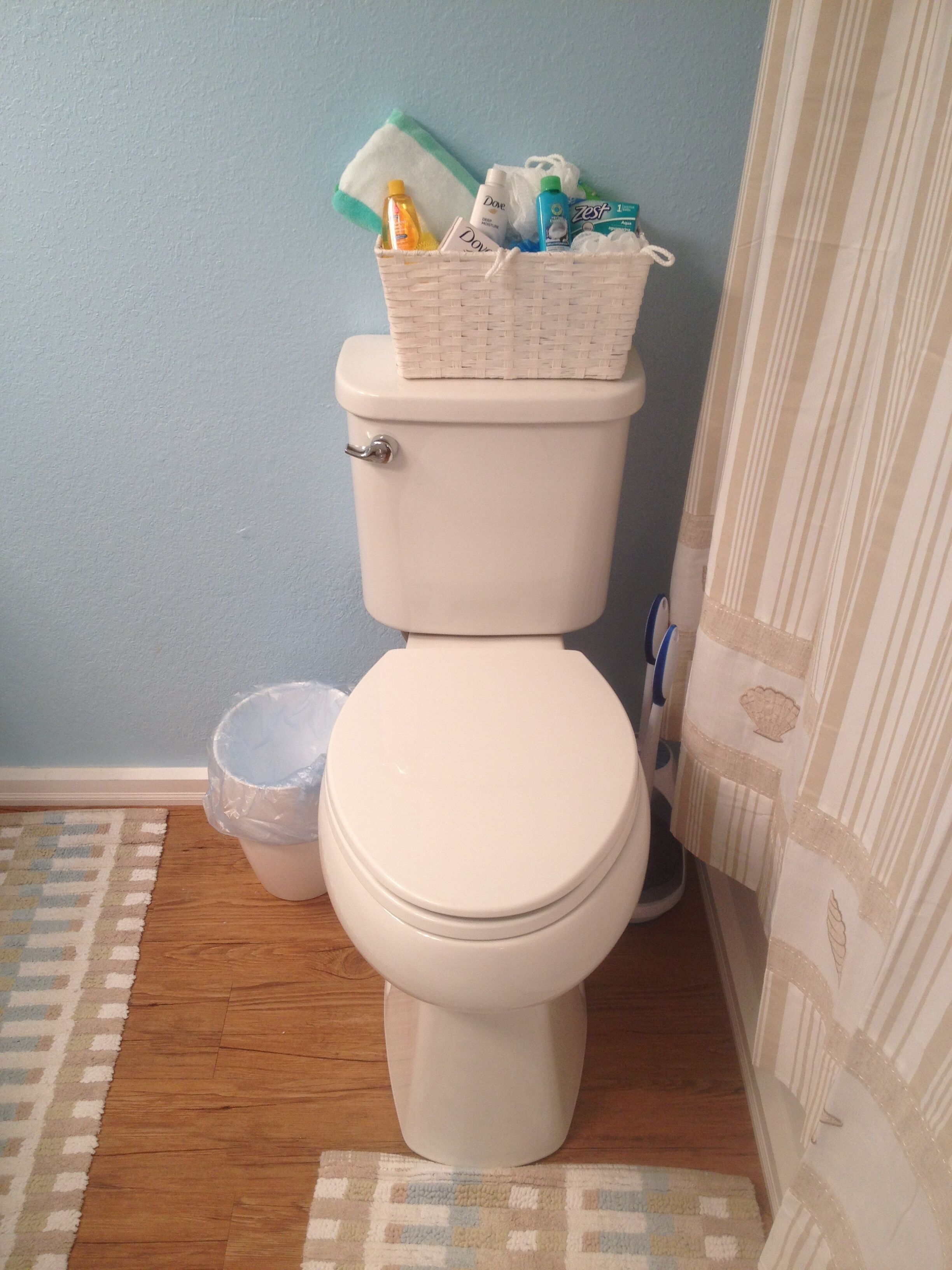 Ein Badezimmer mit einer weißen Toilette, einem Korbwäschekorb auf dem Tank, einem Mülleimer und einem gemusterten Teppich.