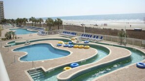 A pool area with multiple swimming pools and lounge chairs, overlooking a beach.