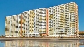 A high-rise hotel with multiple balconies, located near a body of water.