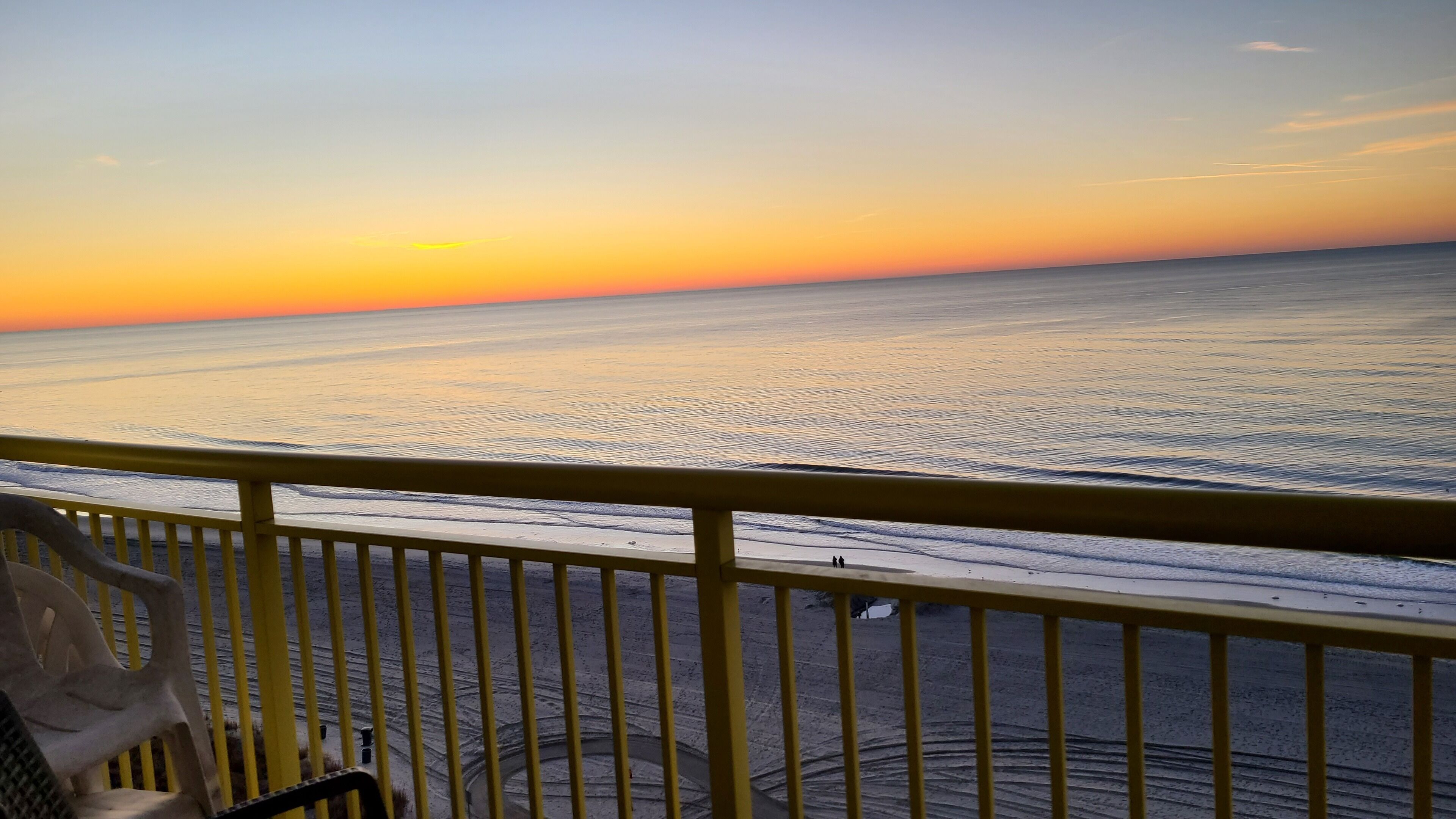 A balcony with a view of the ocean at sunset.