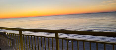 A balcony with a view of the ocean at sunset.