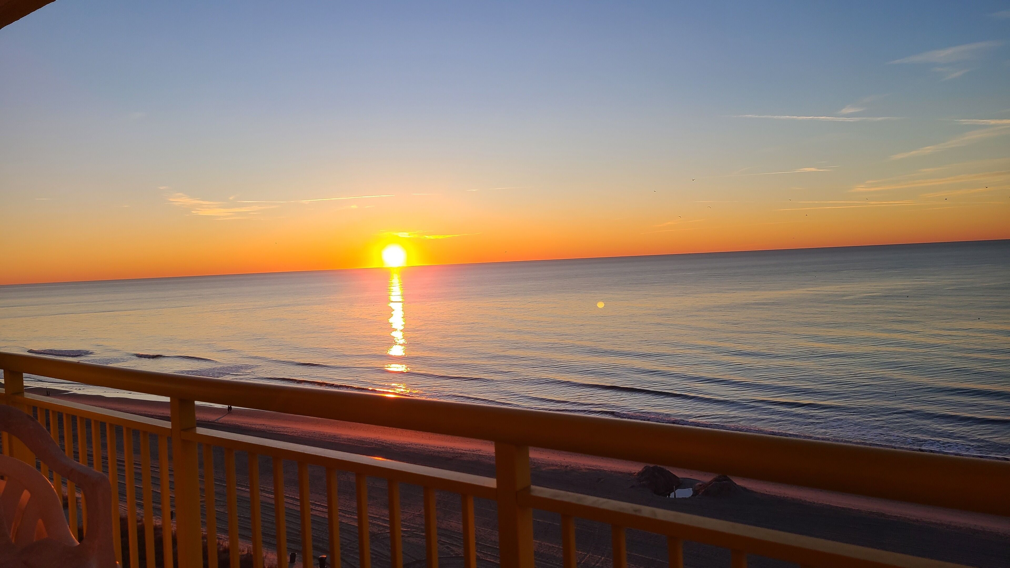 Ein Sonnenuntergang über ruhigem Meer, betrachtet vom Balkon mit Geländer.