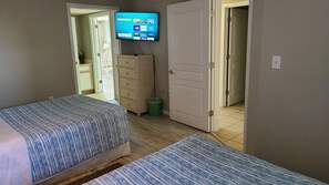 Quarto de hotel com uma cama, televisão fixada na parede, penteadeira e porta que dá para outro espaço.