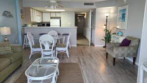 A modern living room with a dining area, kitchen, and a hallway leading to a bedroom.
