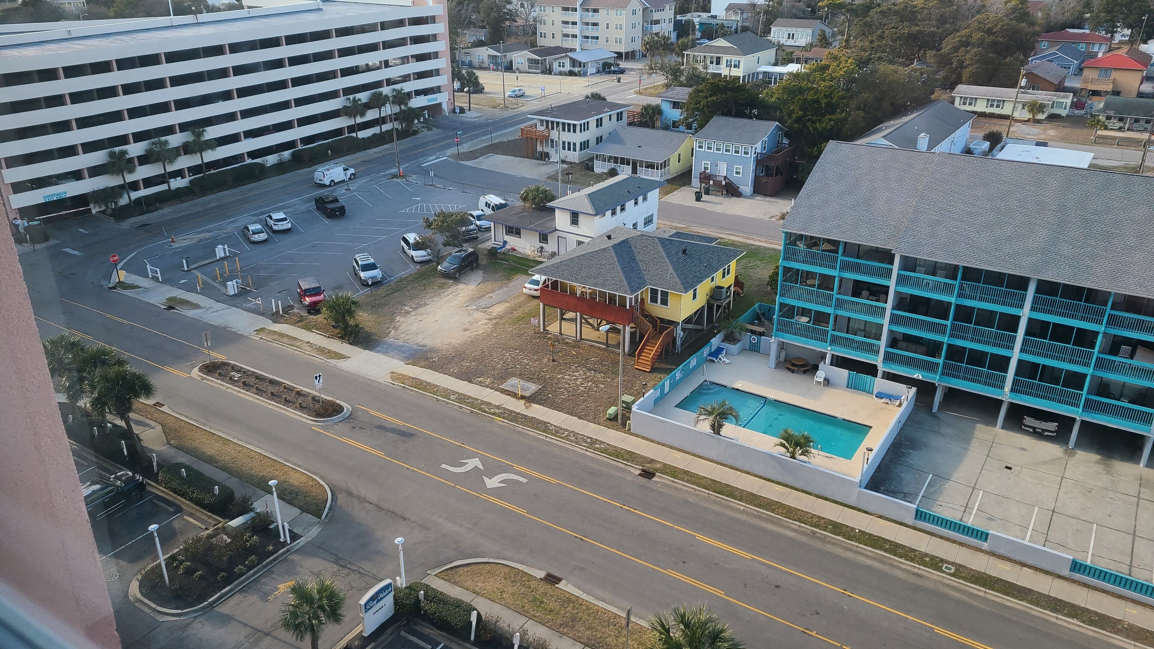 A multi-story building with a swimming pool, a parking lot, and a street with cars.