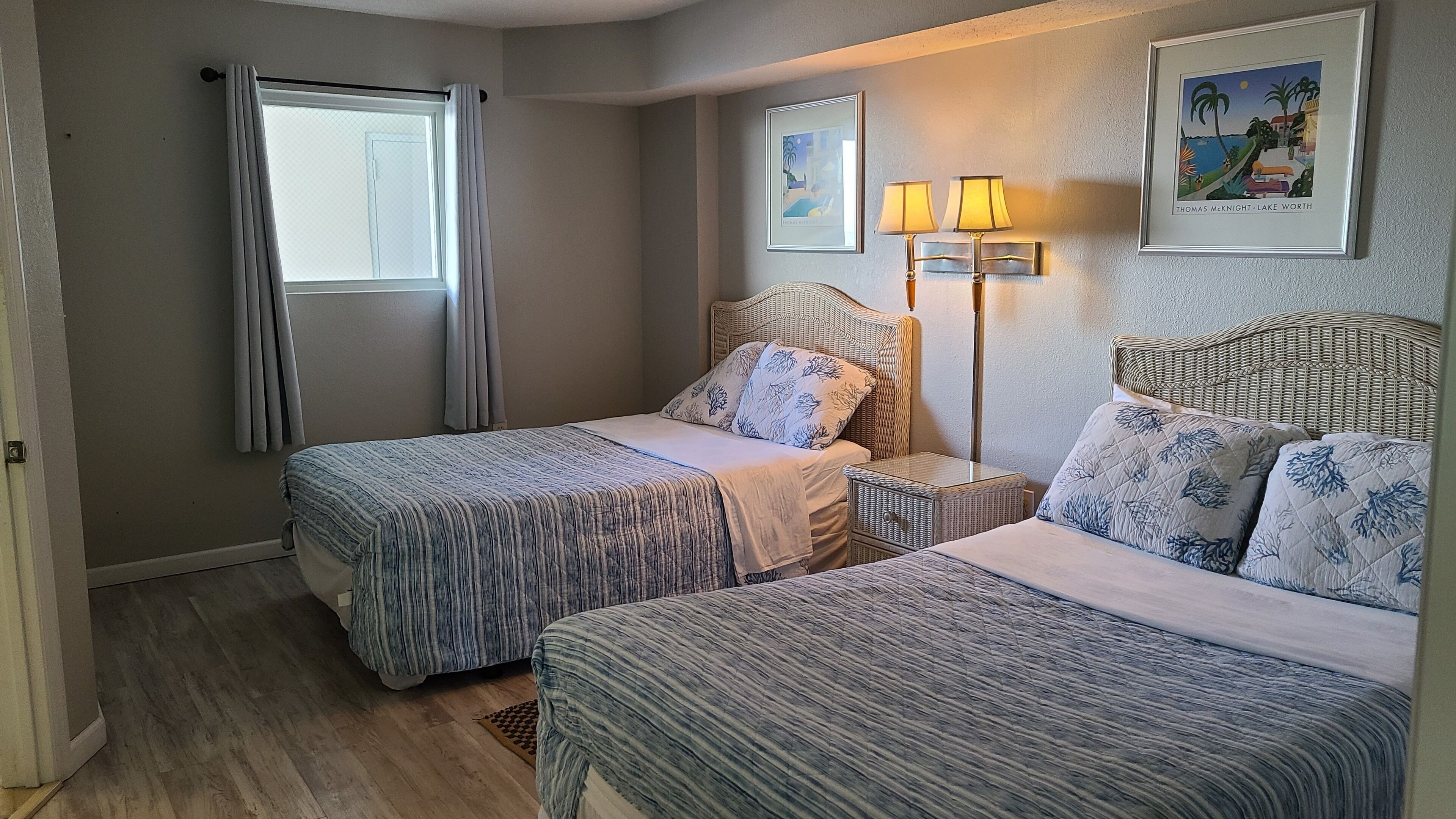 Een hotelkamer met twee bedden, een raam met gordijnen, een wandlamp en een ingelijst schilderij.