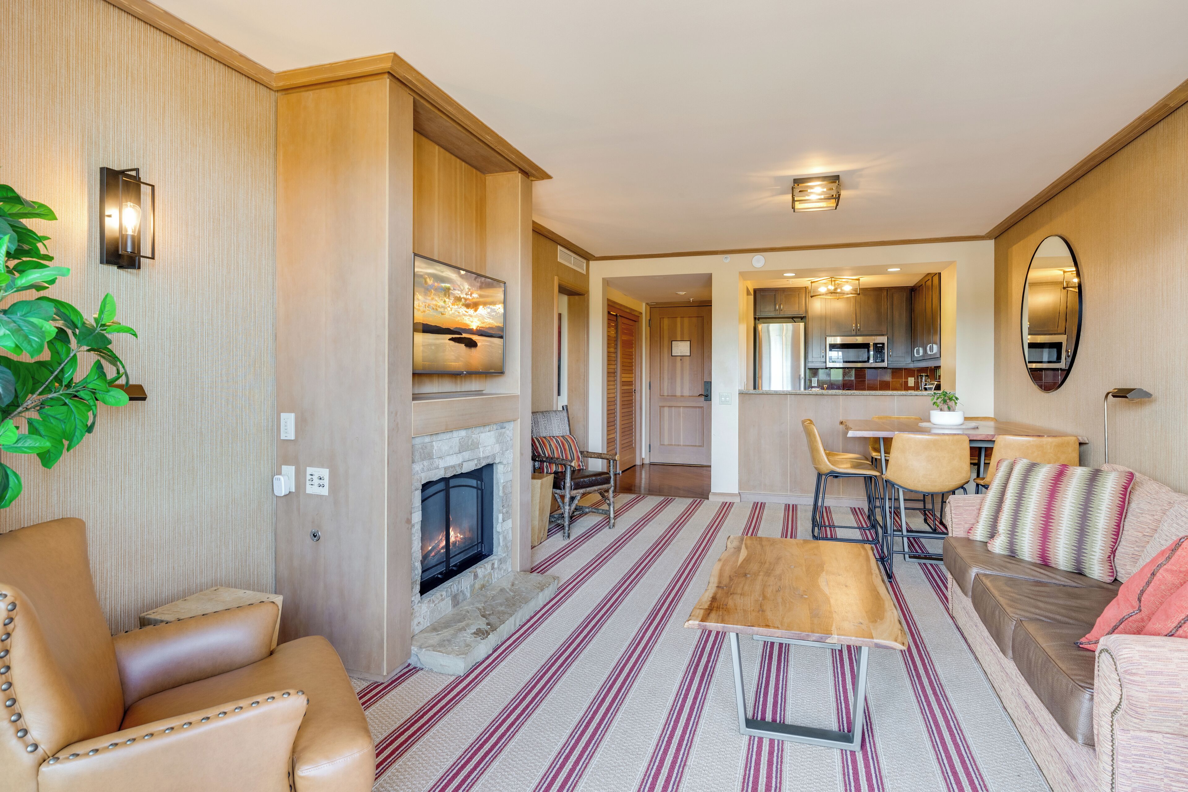 A modern living room with a fireplace, leather sofas, a striped rug, and a dining area with a kitchen visible in the background.
