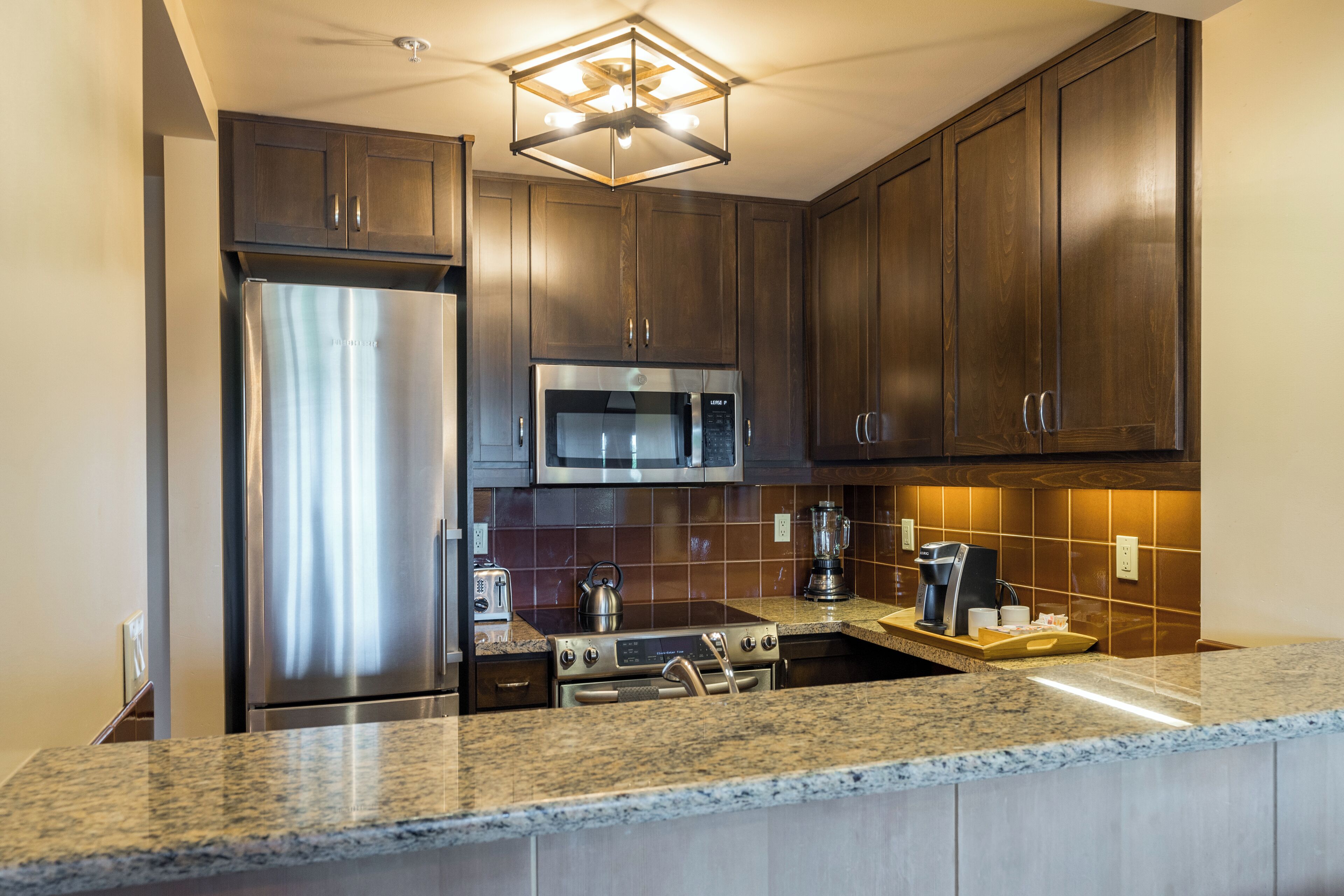 A modern kitchen with dark wood cabinets, stainless steel appliances, and a granite countertop.