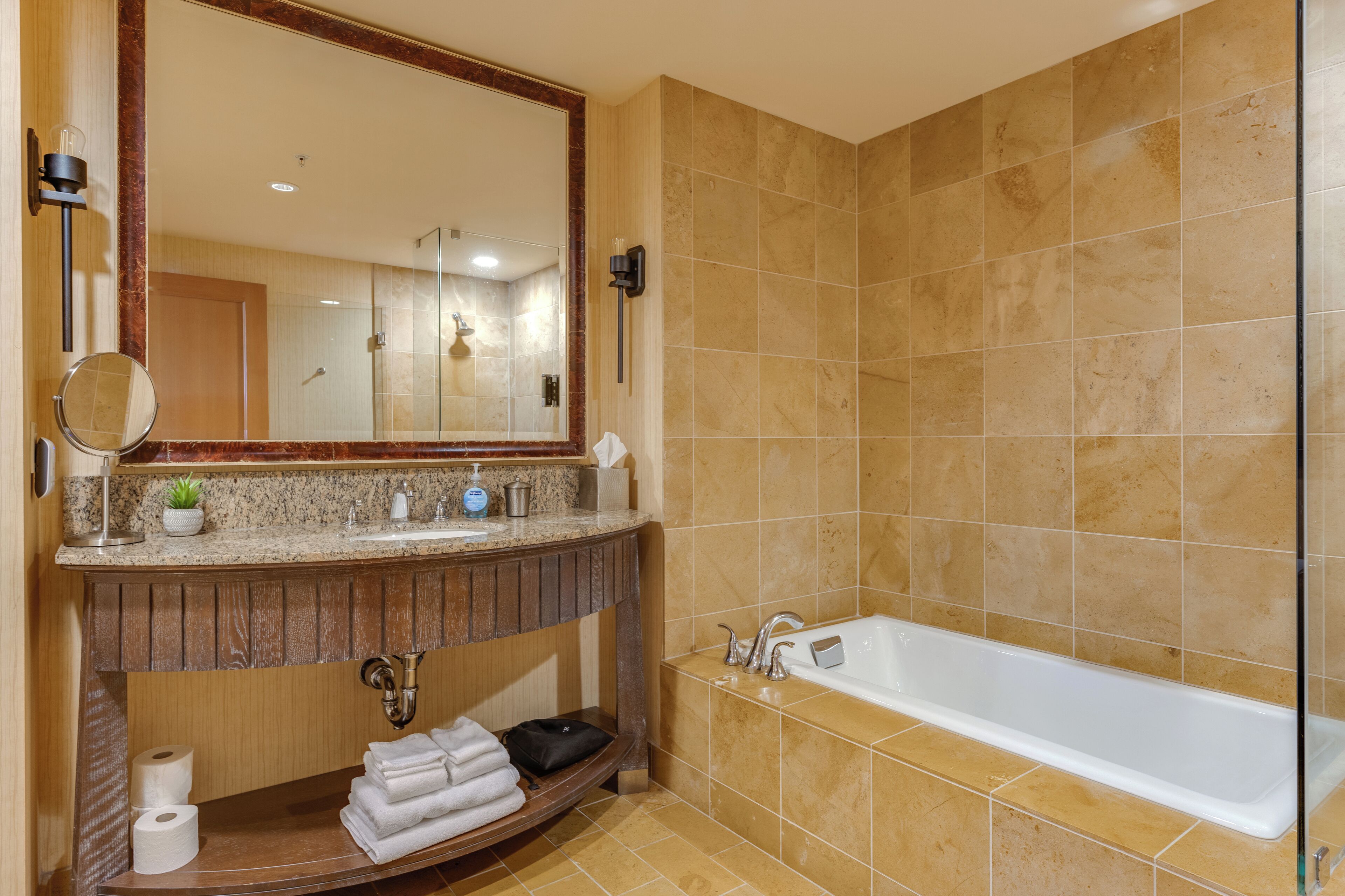 A bathroom with a large mirror, a sink with toiletries, a towel rack, and a bathtub.