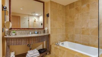 A bathroom with a large mirror, a sink with toiletries, a towel rack, and a bathtub.