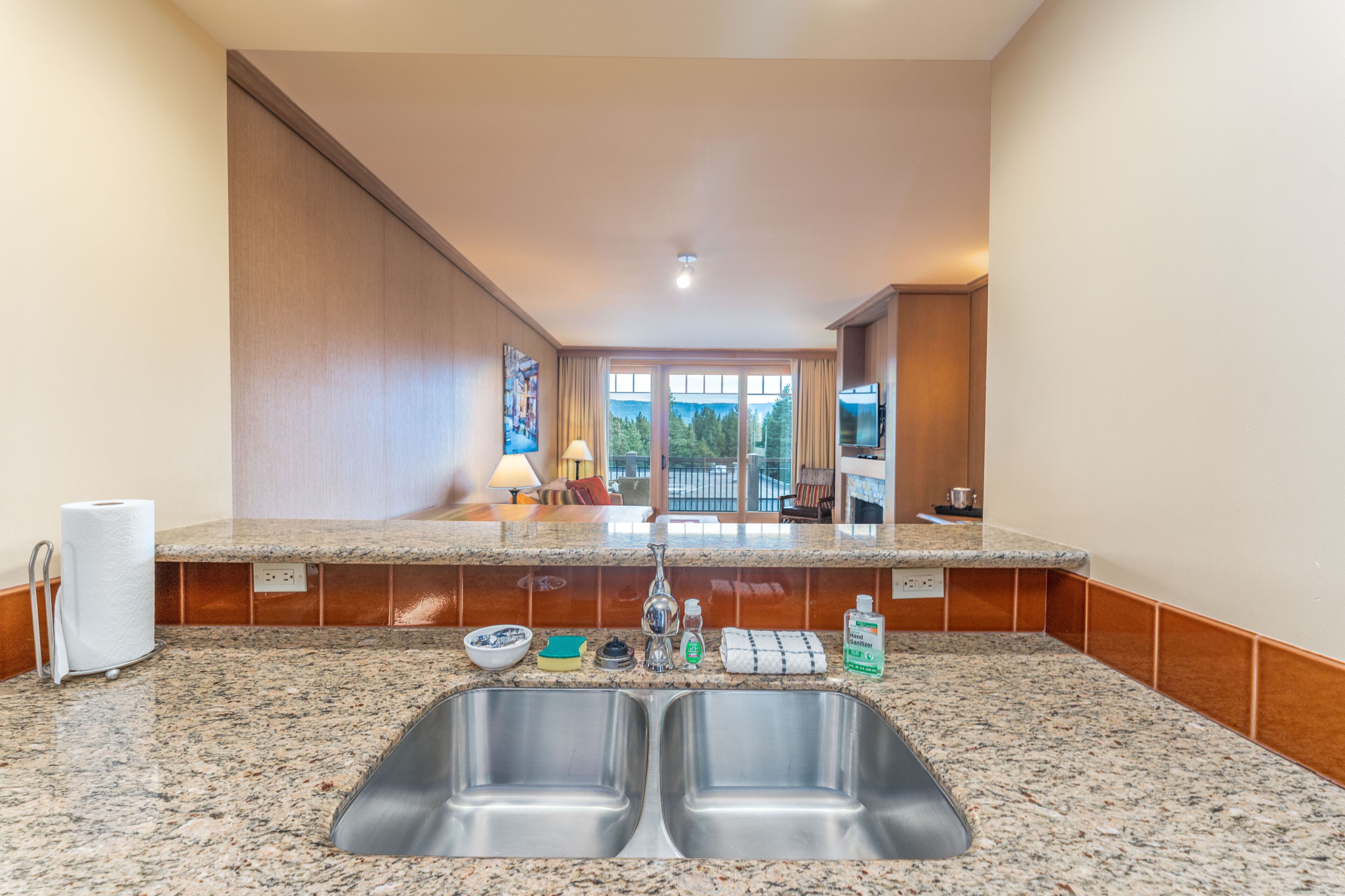 A kitchen with granite countertops, stainless steel sinks, and a view of the outdoors through large windows.