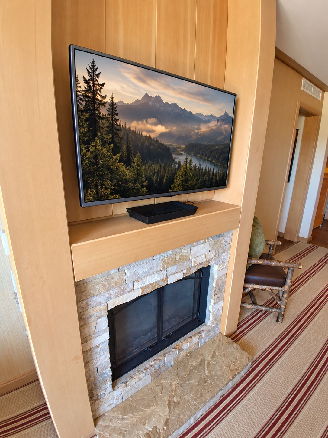 A flat-screen TV mounted above a stone fireplace with a scenic view of a forest and mountains.