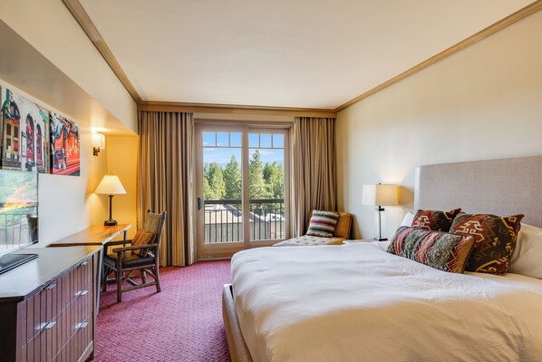 A hotel room with a bed, a desk, a chair, a window with curtains, and artwork on the wall.