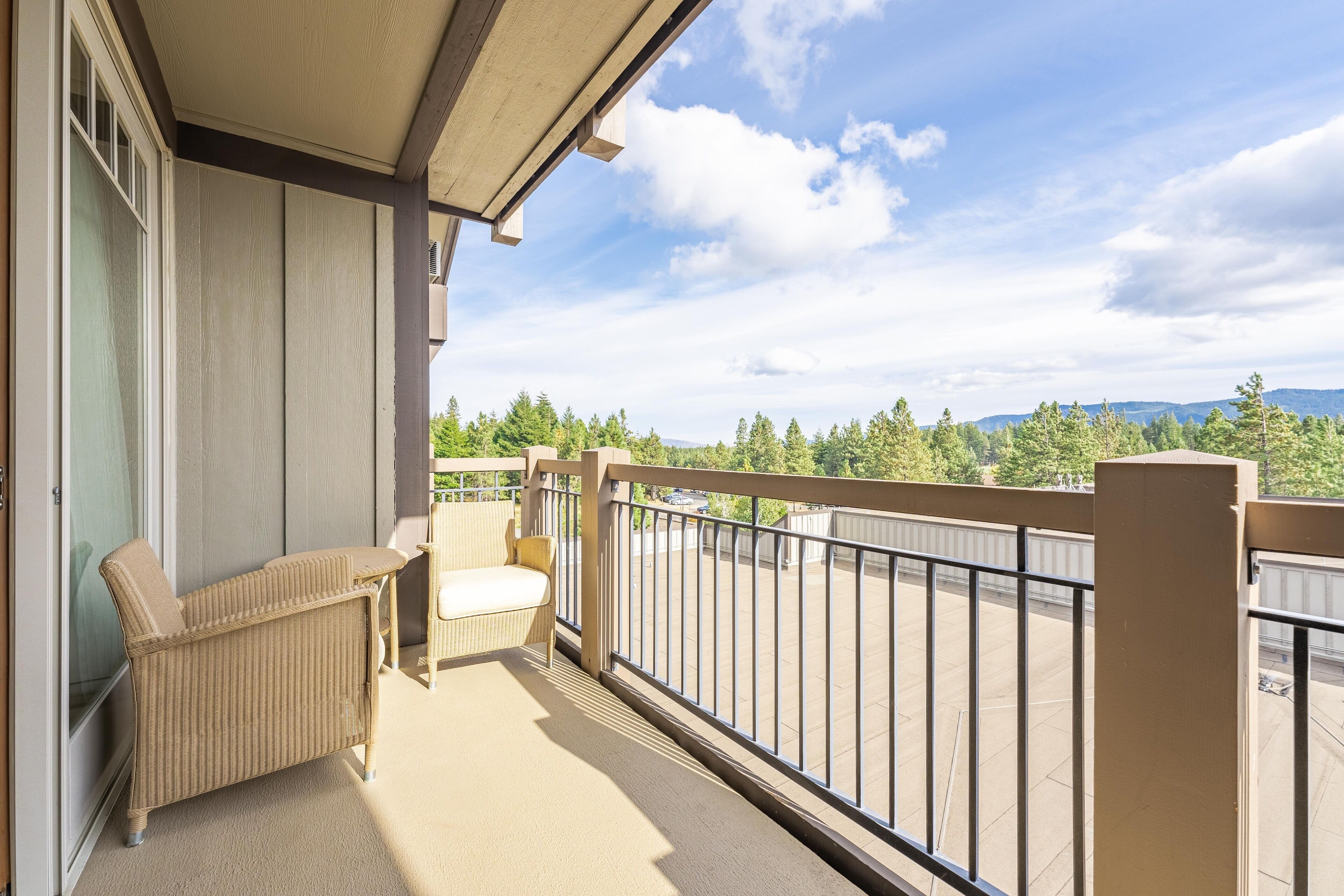 A balcony with a wicker chair and a sofa, a railing, and a view of trees and mountains.