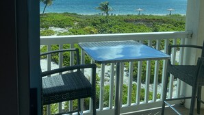 A balcony with a view of the ocean, a table, and two chairs.