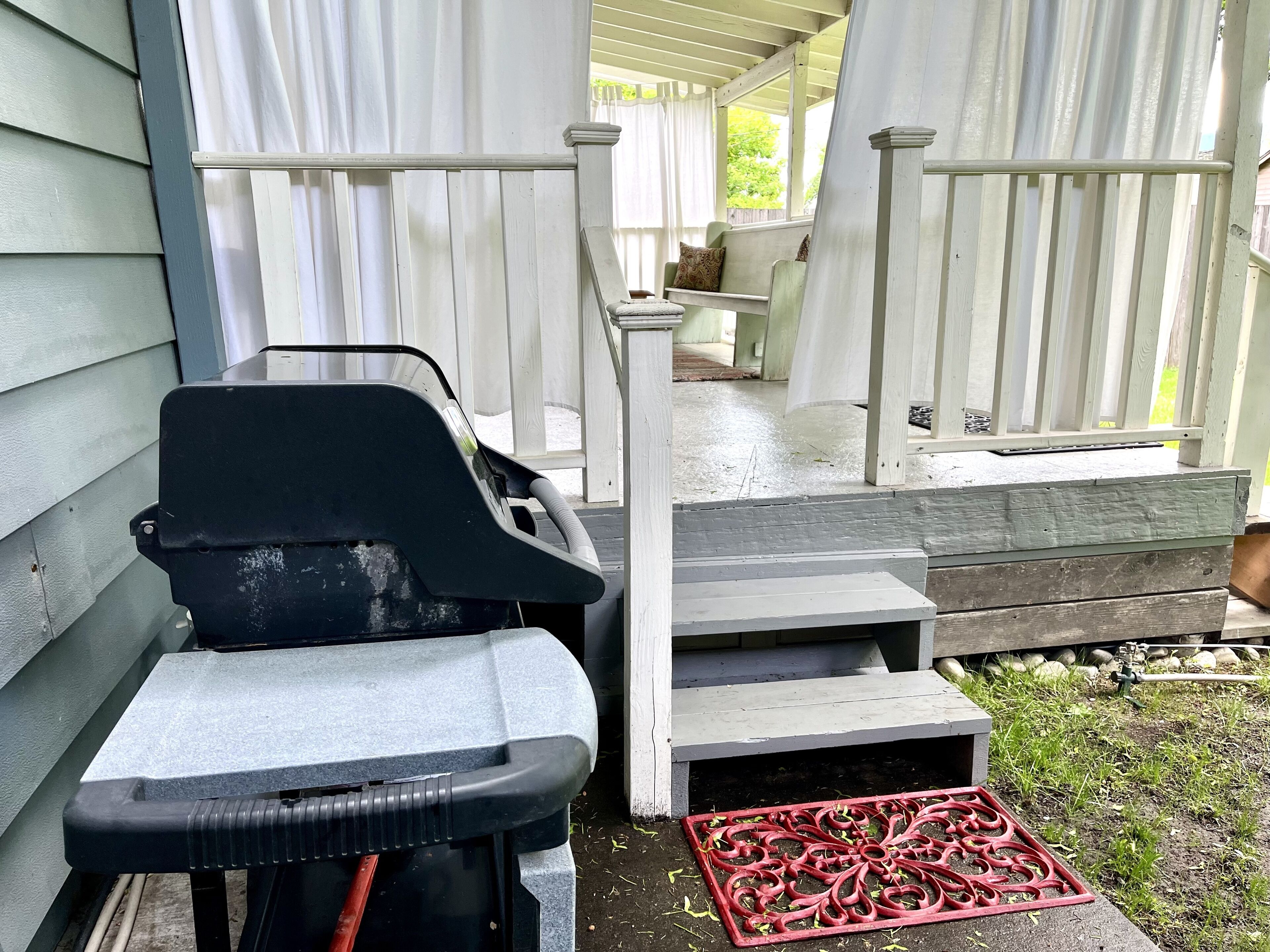 A covered outdoor area with a grill, steps leading to a porch, and a red decorative metal piece.