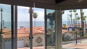 Une pièce dotée de grandes portes vitrées donnant sur un balcon avec vue sur la mer et les palmiers.