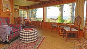 A cozy cabin interior with a plaid sofa, round ottoman, and wooden dining table. - Gorgeous Ocean View! Private. Cozy Comfort. (Neskowin)