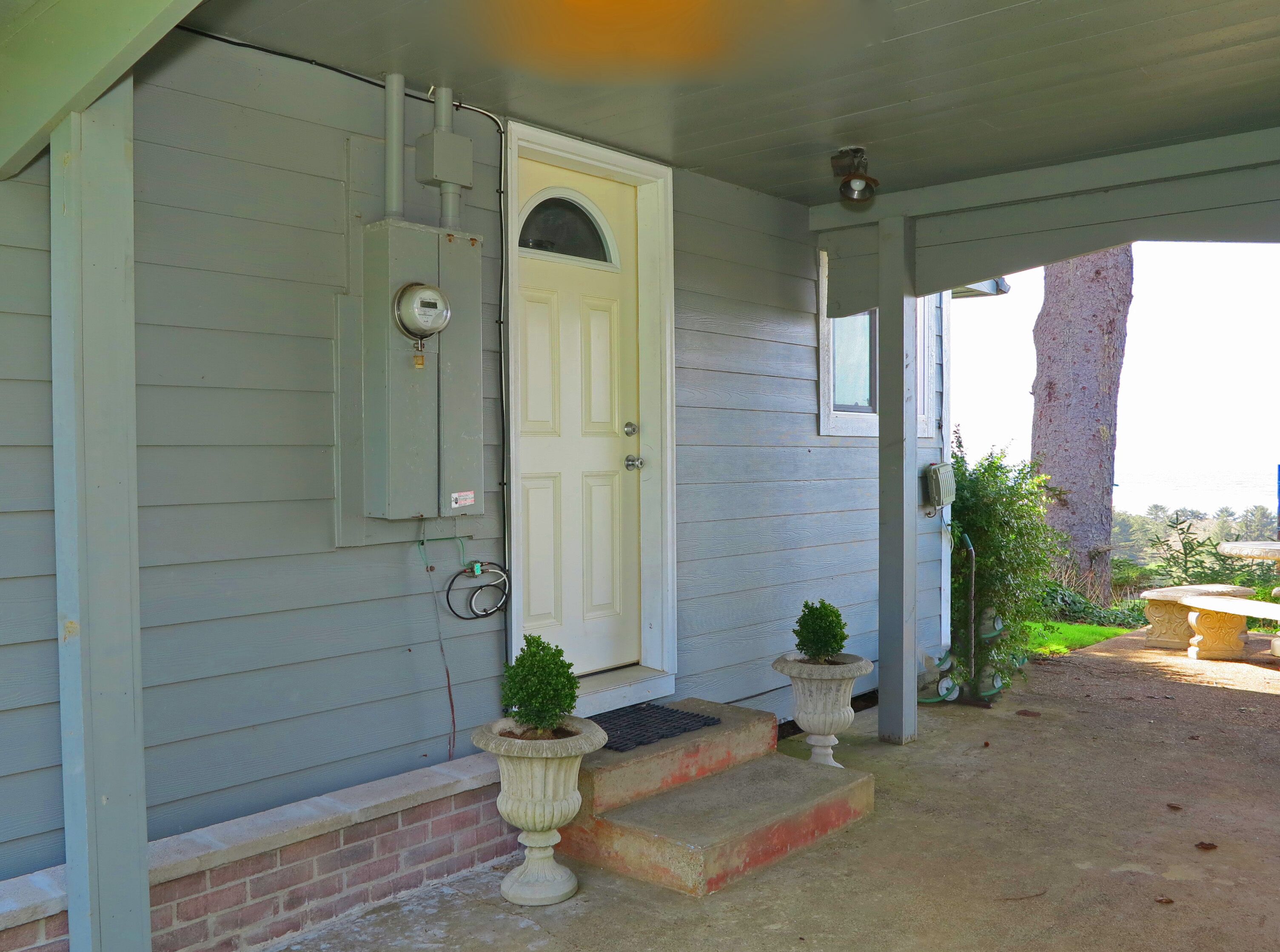 A house with a white door, a small porch with steps, and a stone planter with a shrub.