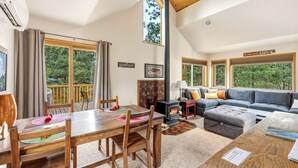 L’intérieur chaleureux d’un chalet comprend un coin repas, un canapé, une cheminée et de grandes fenêtres donnant sur une forêt.