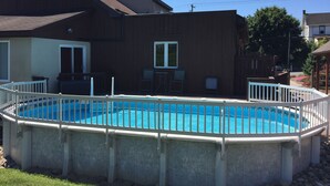 A swimming pool with a white fence, a wooden deck, and a house in the background.