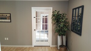 A hallway with a white door, a potted plant, and a framed picture on the wall.