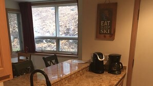 A kitchen with granite countertops, stainless steel sink, and wooden cabinets. There is a window with blinds, a coffee maker, and a sign on the wall. - Seasons On Mount Snow - Ski-in/Ski-out  (Dover)
