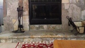 A stone fireplace with a mantel shelf, a black fire screen, and two decorative items. - Seasons On Mount Snow - Ski-in/Ski-out  (Dover)